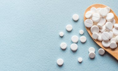 Beyaz haplar, mavi masadaki tahta kaşıkta tabletler. Tıp ve sağlık konsepti. Eczacılık. Üst Manzara. Haplar ve vitaminler.