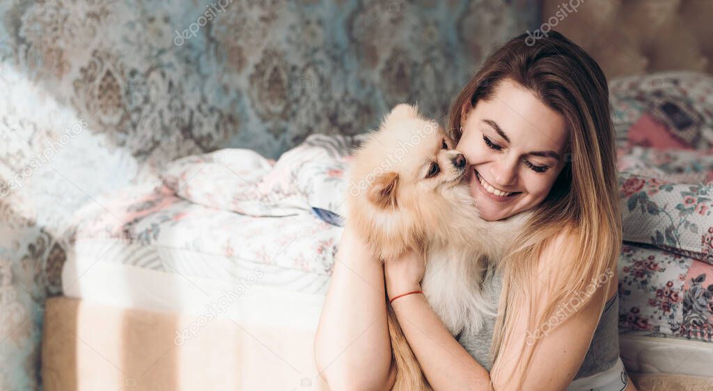 Pretty young female model, happy girl owner of a dog playing with a pomeranian spitz. Cute couple have fun. Dog lover with pet