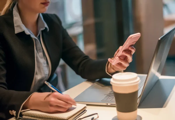 Genç bir kadın ahşap bir masada kahve masasında oturuyor. Masada bir dizüstü bilgisayar var. Kız internette geziniyor, sohbet ediyor, blog yazıyor. Defterde telefonu tutan ve yazan kadın.