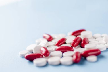 Mavi tıbbi arka planda beyaz haplar ve kırmızı kapsüller yığını