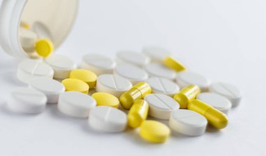 Beyaz arka planda izole edilmiş sarı ve beyaz kapsüllerden oluşan kavanoz ve yığın. Tıbbi konsept