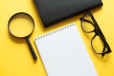 Sarı arka planda not defteri, büyüteç ve siyah gözlüklü iş konsepti
