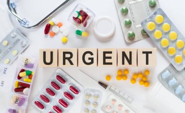 Tahta bloklara acil bakım kelimesi yazılmış. Arka planda haplar, vitaminler, steteskop ve şırınga ile tıbbi konsept.