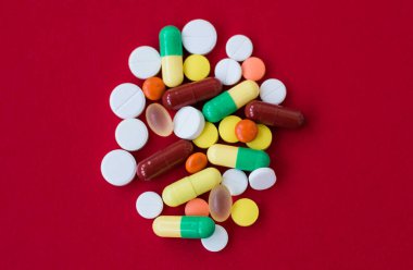 Kırmızı arka planda ilaç ve kapsül içeren tıbbi geçmiş. Çeşitli ilaç hapları, tablet. Çeşitli ilaç tabletleri ve haplar farklı renklerde. Sağlık hizmetleri. Üst görünüm
