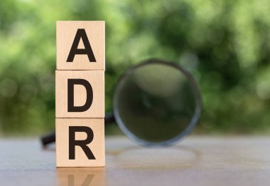 ADR Abbreviation On Wooden Blocks on table with magnifier on green background clipart