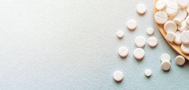 Beyaz haplar, mavi masadaki tahta kaşıkta tabletler. Tıp ve sağlık konsepti. Eczacılık. Üst Manzara. Haplar ve vitaminler.