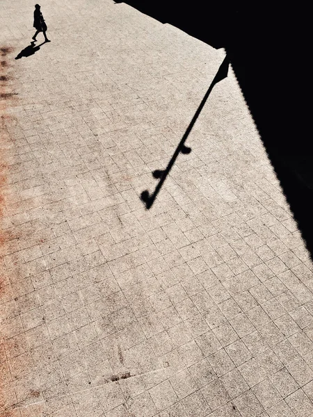 Bir kişi binanın gölgesinde, kaldırımda yürüyor..
