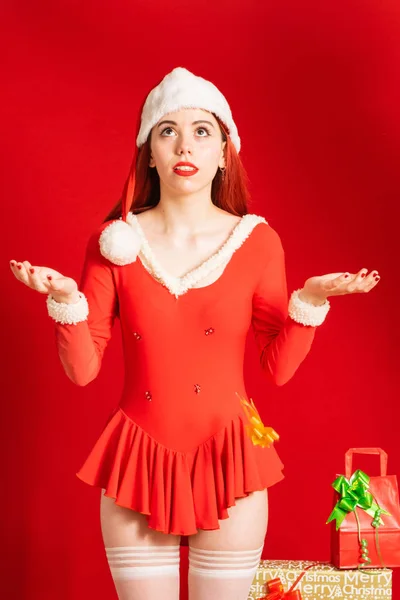 Young and pretty red head girl in a Santa Claus mini dress on a neutral red background.