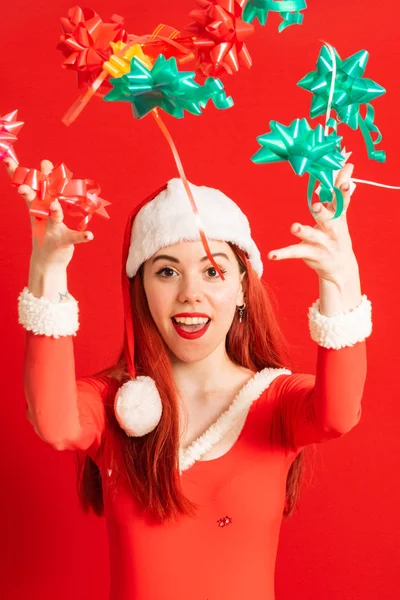 Young and pretty red head girl in a Santa Claus mini dress on a neutral red background.