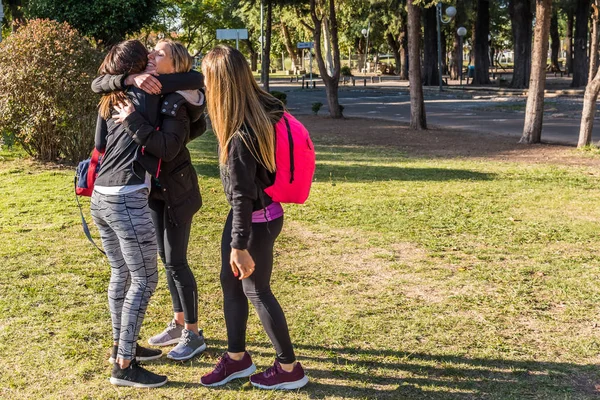 Three young women meet in the park, they greet each other and are happy to meet