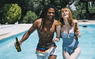 Elinde bira şişeleri ile havuzda multiracial çift ve gülümseyerek