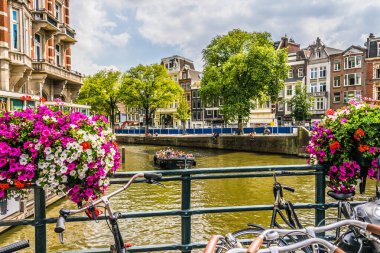 Amsterdam, Hollanda - 18 Temmuz 2018: Amsterdam 'daki kanallardan birinin görüntüsü. Çok çiçekli bir köprü ve bir yaz öğleden sonra sokaklarda bir sürü turist.