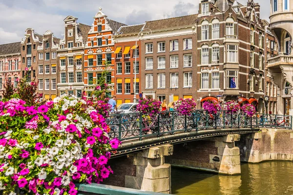 Amsterdam, 18 juli 2018: Typische brug over een kanaal met veel fietsen en bloemen. — Stockfoto