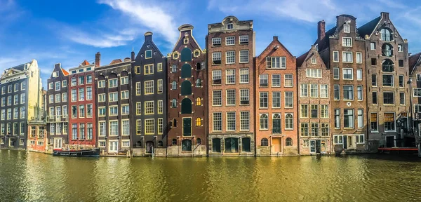 Panoramautsikt över typiska nederländska hus vid Amsterdamkanalen Damrak på solig dag, Nederländerna. — Stockfoto