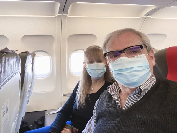 Yetişkin çift, salgın sırasında uçakla seyahat ederken cerrahi maske takarak selfie çekiyor..