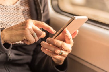 Yetişkin bir kadının elleri trende cep telefonuna mesaj yazmak üzere.