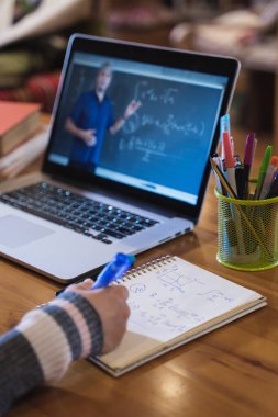 Öğrenci, evden Matematik öğretmeniyle çevrimiçi video dersi izlerken not alıyor
