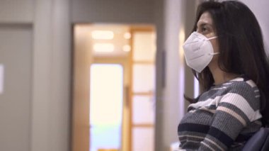 Yüzü maskeli genç bir kadın hastanede boş bir bekleme odasında oturuyor. Endişeli kız Coronavirus salgını sırasında doktoru ziyaret ediyor.