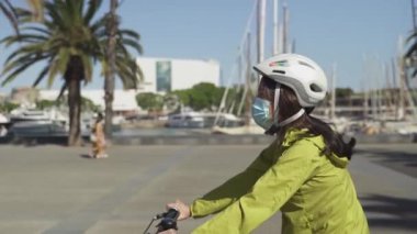 Barcelona Limanı 'nın ünlü turistik bölgesinde bisiklet süren maske takan genç bir kadın. Coronavirus tecridi yüzünden neredeyse terk edilmiş bir şehir.