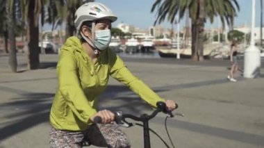 Yüz maskesi takan genç bir kadın, Coronavirus krizi nedeniyle boş turistik Barcelona kentinin liman bölgesinde bisiklet sürüyor.