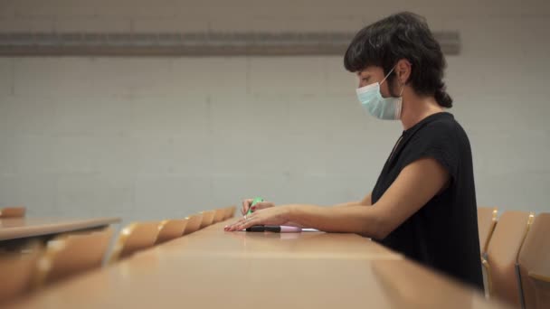 Kobieta w masce na twarzy, siedząca w pustej klasie z powodu pandemii koronawirusowej. Nowe środki normalizacyjne w edukacji — Wideo stockowe