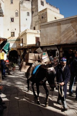 Fas 'taki Old Fez Medina' da Seffarine Meydanı 'nda eşeğin üzerinde mal taşıyan tüccarlar var..
