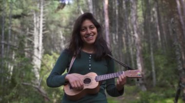 Mutlu Gülen Genç Kadın Ormanın ortasında Ukelele şarkısı çalıyor