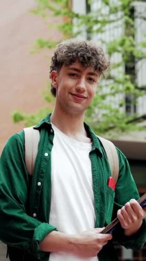 Üniversite kampüs binasında dikilen gülümseyen öğrencinin portresi, konferansa hazır kameraya mutlu bir şekilde bakıyor.