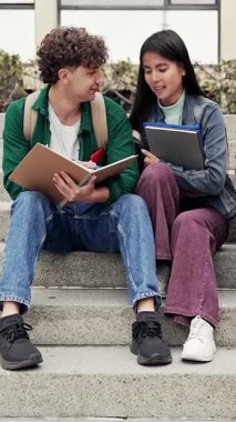 İki üniversite öğrencisi basamaklarda oturuyor ve notlarını paylaşıyor, birbirlerine akademik sınavlar için yardım ediyorlar