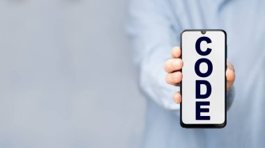 Mavi gömlekli bir adam elinde mavi arka planda mesaj kodlu bir akıllı telefon tutuyor.