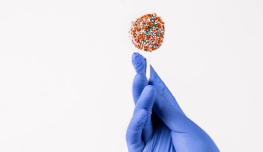 Elinde renkli şekerler olan mavi cerrahi eldivenlerle insan elinin yakın çekimi. Beyaz arka planda izole edilmiş. Metnin için boşluk kopyala