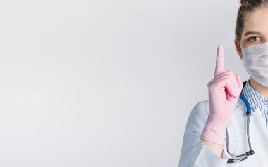 Beyaz önlüklü ve pembe steril eldivenli güzel kadın doktor, beyaz arka planda parmak izi olan bir işaret gösteriyor..