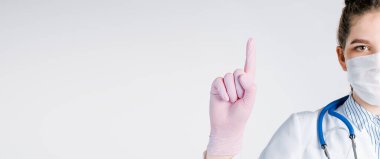 Beyaz önlüklü ve pembe steril eldivenli güzel kadın doktor, beyaz arka planda parmak izi olan bir işaret gösteriyor..