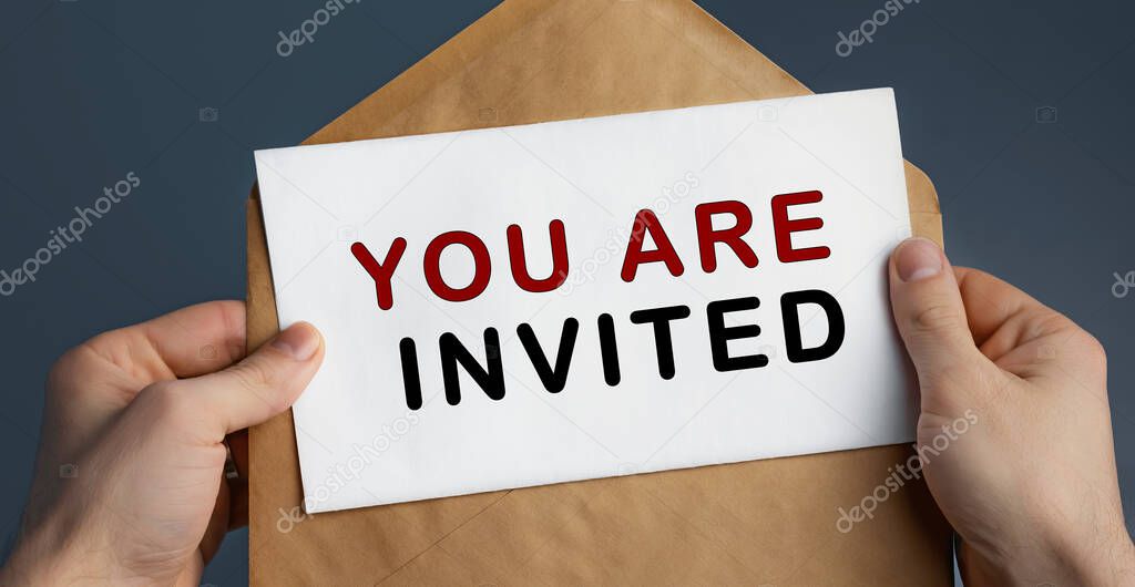 Cropped view of man holding craft envelope with text YOU ARE INVITED on blue background
