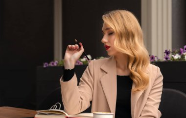 Uzun sarı saçlı, kahve içip günlük, kitap ya da notlar yazan genç ve güzel bir kadın..