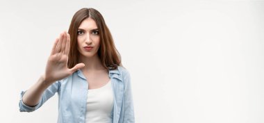 Uzun kestane rengi saçları olan ciddi bir kız, gündelik kıyafetlerle giyinmiş, eli ile durduğunu gösteriyor, reddedildiğini gösteriyor, şiddete, vücut diline izin vermiyor. İnsani duygular, yüz ifadesi kavramı.