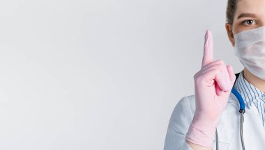 Beyaz önlüklü ve pembe steril eldivenli güzel kadın doktor, beyaz arka planda parmak izi olan bir işaret gösteriyor..