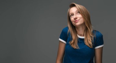 Sarışın, güzel bir kadının stüdyo fotoğrafı. Mavi tişört giyiyor, gizemli bakışlar atıyor. Yasadışı ya da gizlice bir şeyler yapmak istiyor.