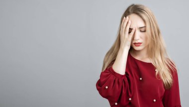 Uzun sarı saçlı yorgun Avrupalı genç bir kadının fotoğrafı, yüzünü kapatıyor, gözlerini kapatıyor, yorgunluk hissediyor, dinlenmeye ihtiyacı var, uykulu bir ifadeye sahip, gri arkaplan üzerinde izole edilmiş. Yorgunluk ve insanlar