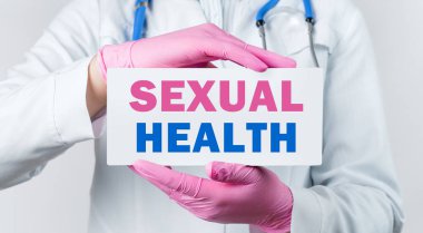 Beyaz önlüklü ve pembe steril eldivenli genç bir kadın doktorun cinsel sağlık kartı taşıdığı görüntüler. Tıbbi konsept.