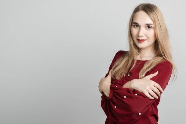 Aşk, şefkat konsepti. Çekici Avrupalı genç bir kadın, uzun sarı saçları ayakta, kollarını göğsünde birleştirmiş, gri arka planda. Metnin için boşluk kopyala