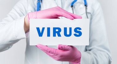 Beyaz önlüklü ve pembe steril eldivenli genç bir kadın doktorun elinde VIRUS yazılı bir kart tutarken çekilmiş görüntüsü. Tıbbi konsept.