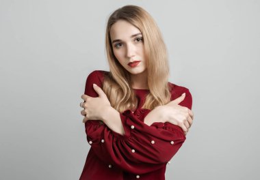 Aşk, şefkat konsepti. Çekici Avrupalı genç kadın, uzun sarı saçları ayakta, kollarını göğsünde birleştirmiş, gri arka planda.