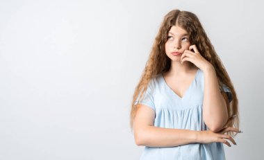 Dalgın Avrupalı, uzun kıvırcık saçlı genç bir kadının fotoğrafı. Düşünceli bir ifadeyle yukarı bakıyor. Beyaz arka planda izole edilmiş. Metnin için boşluk kopyala