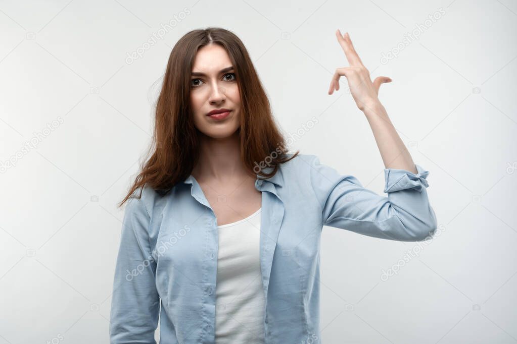 Unhappy caucasian Young woman with long chestnut hair, dressed in casual clothes, tilts head, imitates gun shoot, makes suicide gesture, has puzzled expression. Human emotions concept.