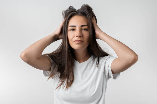 Довольно беззаботная современная девушка с длинными каштановыми волосами, прижатыми к голове или трогательными волосами. Изолированный на белом фоне. Выражения, выражения, прическа и концепция людей.
