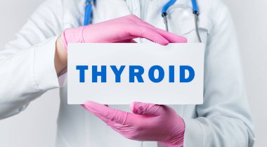 Beyaz önlüklü ve pembe steril eldivenli genç bir kadın doktor, THYROID yazılı bir kart tutuyor. Tıbbi konsept.