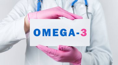Beyaz önlüklü ve pembe steril eldivenli genç bir kadın doktor OMEGA-3 yazılı bir kart tutuyor. Tıbbi konsept.