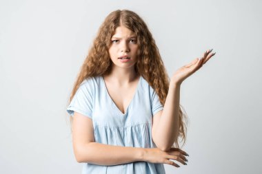 What the hell are you talking about, nonsense. Studio shot of frustrated female with curly long hairstyle gesturing with raised palm, frowning, being displeased and confused with dumb question.