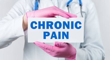Beyaz önlüklü ve pembe steril eldivenli genç bir kadın doktorun elinde CHRONIC PaIN yazılı bir kart tutarken çekilmiş görüntüsü. Tıbbi konsept.